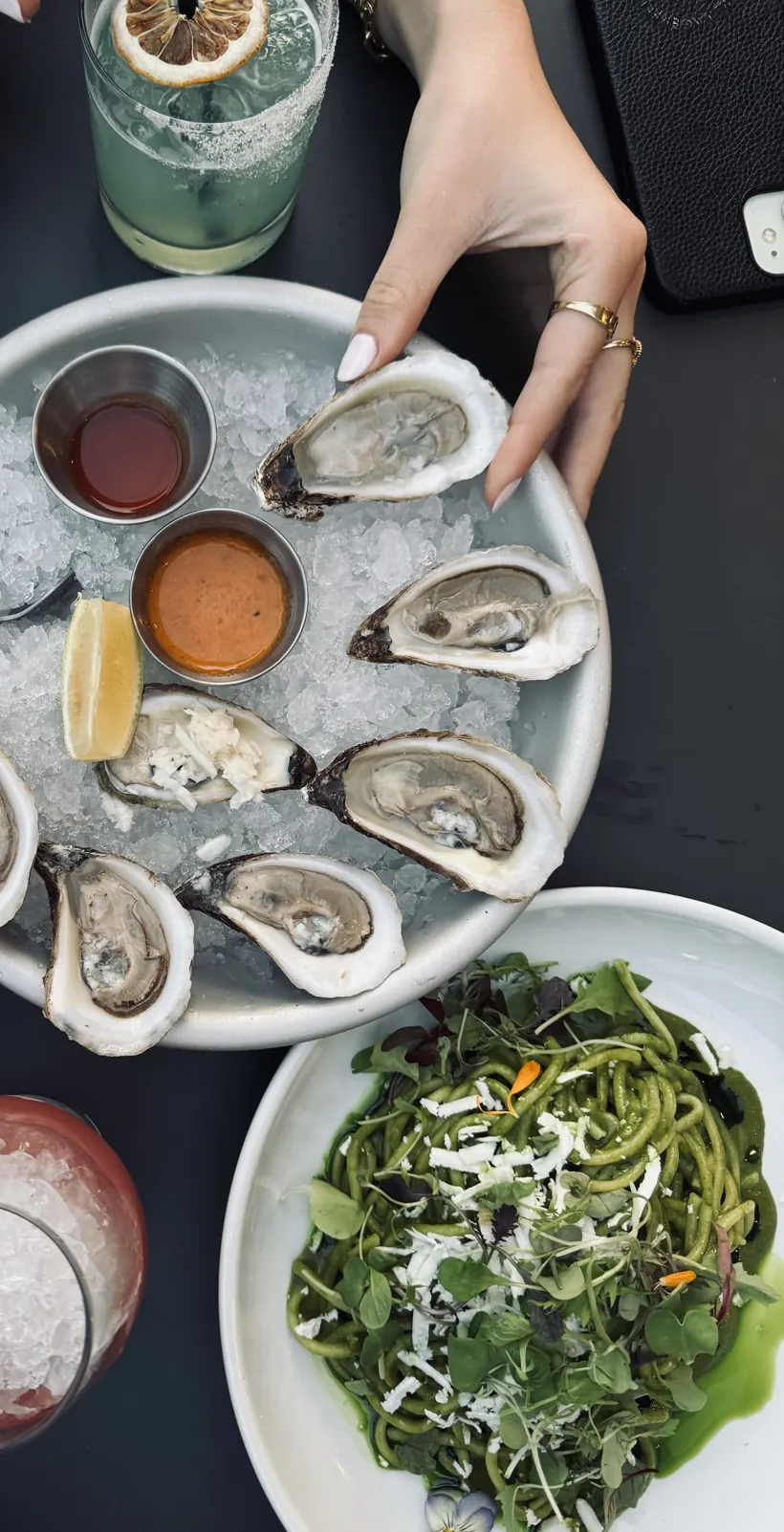 Overhead terrasse spread: oysters on ice, cocktails, fries and a green pasta